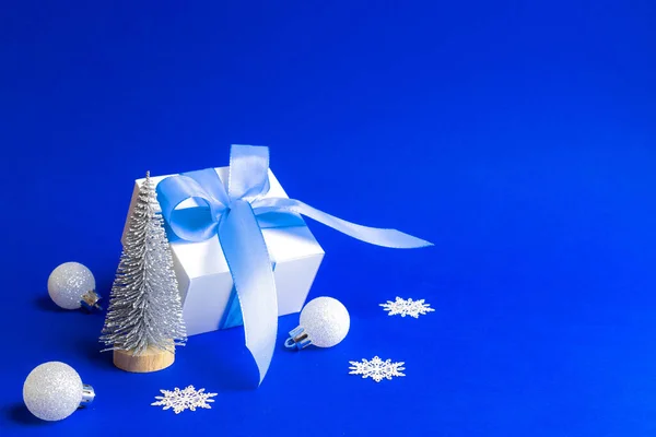 Świąteczne Dekoracje Niebieskie Tło Białe Pudełko Niebieską Wstążką Drzewo Zimowe — Zdjęcie stockowe