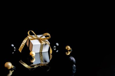 Noel indirimi. Altın yaylı beyaz hediye, altın toplar ve yeni yıl ağacı. Koyu arkaplanda tebrik kartı için. Uzayı kopyala Kış tatili, yeni yıl