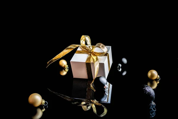 Nastro regalo oro. Confezione regalo bianca con nastro dorato, palline di Capodanno e albero invernale in composizione natalizia su sfondo nero per biglietto di auguri. Composizione festiva invernale con spazio copia. — Foto Stock