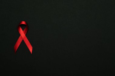 Kanser kurdeleleri. HIV dünyasında siyah zemin üzerinde kırmızı kurdele sembolü. Farkındalık yardımcıları ve kanser. Düz konum, üst görünüm, kopyalama alanı.