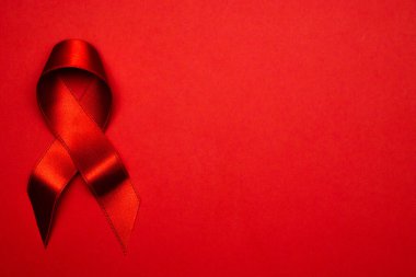 Kanser kurdeleleri. HIV dünyasında kırmızı arkaplanda kırmızı kurdele sembolü. Farkındalık yardımcıları ve kanser. Düz konum, üst görünüm, kopyalama alanı.