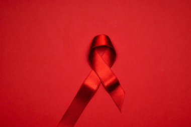 Kanser kurdeleleri. HIV dünyasında kırmızı arkaplanda kırmızı kurdele sembolü. Farkındalık yardımcıları ve kanser. Düz konum, üst görünüm, kopyalama alanı.