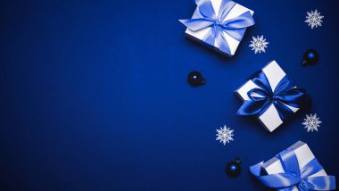 Xmas dekorasyonu. Cyan papyonlu beyaz hediye, mavi toplar ve Noel süslemesinde tebrik kartı olarak mavi arka planda kış ağacı. Düz konum, üst görünüm, kopyalama alanı