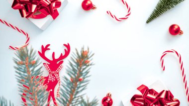 Hediye kurdele kutusu. Kırmızı kurdeleli beyaz hediye kutusu, yeni yıl baloları, Noel kompozisyonunda şeker ve kış ağacı tebrik kartı için beyaz arka planda. Noel, kış, yeni yıl konsepti