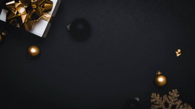 Sürpriz hediye. Altın kurdeleli beyaz hediye kutusu, yeni yıl baloları ve ışıl ışıl ışık çelenkleri tebrik kartı için siyah arka planda. Düz konum, üst görünüm, kopyalama alanı