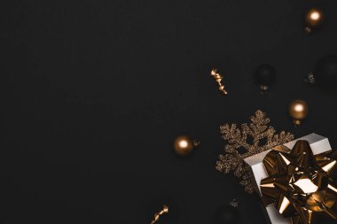 Kış altın madeni. Altın yay, altın toplar ve parlak ışık çelenkleriyle dolu beyaz bir hediye. Karanlık arka planda tebrik kartı için. Kopya alanına sahip kış şenliği kompozisyonu