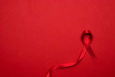 Kanser kurdeleleri. HIV dünyasında kırmızı arkaplanda kırmızı kurdele sembolü. Farkındalık yardımcıları ve kanser. Düz konum, üst görünüm, kopyalama alanı.
