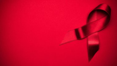 Kurdele ipeği. HIV dünyasında kırmızı arkaplanda kırmızı kurdele sembolü. Farkındalık yardımcıları ve kanser. Düz konum, üst görünüm, kopyalama alanı.