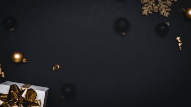 Hediye kurdele altını. Altın kurdeleli beyaz hediye kutusu, yeni yıl baloları ve ışıl ışıl ışık çelenkleri tebrik kartı için siyah arka planda. Düz konum, üst görünüm, kopyalama alanı