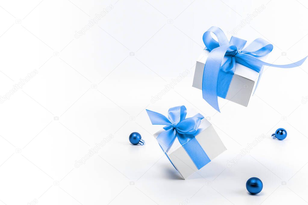 Holiday Christmas background. White gift box with blue ribbon, New Year balls in xmas composition on white background for greeting card. Copy space. Winter holidays, New Year
