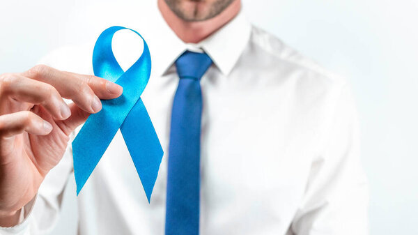 Prostate care. Awareness prostate of men health in November. Hipster men in bright shirt, cyan tie with blue ribbon in hands on white background. World cancer day and world diabetes day concept