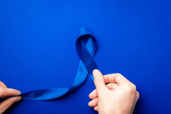 Prostate care. Awareness prostate cancer of men health in November. Blue ribbon in hands isolated on deep blue background. World cancer day and world diabetes day concept