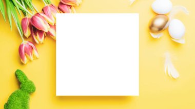 Paskalya çiçeği. Bahar laleleriyle sepetin içinde altın, beyaz yumurta, Mutlu Paskalya dekorasyonunda pastel sarısı arka planda tüyler. Kopyalama alanı olan şenlikli tasarım