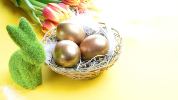 Złote Jaja Koszyku Wiosennymi Tulipanami Białe Pióra Pastelowym Żółtym Tle — Wideo stockowe