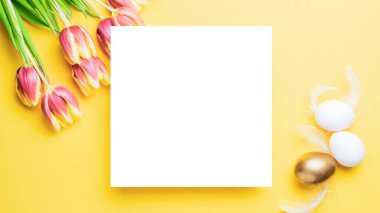 Paskalya bayrağı. Bahar laleleriyle sepetin içinde altın, beyaz yumurta, Mutlu Paskalya dekorasyonunda pastel sarısı arka planda tüyler. Folyo minimalist yumurta tasarımı, modern üst görünüm şablonu.