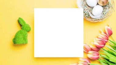 Paskalya sarısı. Bahar laleleriyle sepetin içinde altın, beyaz yumurta, Mutlu Paskalya dekorasyonunda pastel sarısı arka planda tüyler. Düz yatış, üst görünüm