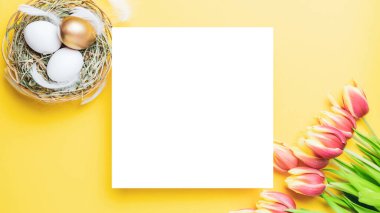 Paskalya bayrağı. Bahar laleleriyle sepetin içinde altın, beyaz yumurta, Mutlu Paskalya dekorasyonunda pastel sarısı arka planda tüyler. Folyo minimalist yumurta tasarımı, modern üst görünüm şablonu