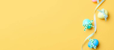 Paskalya geçmişi. Şerit kurdeleli renkli yumurta, bahar laleleri, Mutlu Paskalya dekorasyonunda pastel sarısı arka planda tüyler. Bahar tatili afişi