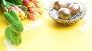 Paskalya yumurtaları altın. Bahar laleli altın rengi yumurta, Mutlu Paskalya dekorasyonunda pastel sarısı arka planda beyaz tüyler. Tebrikler Paskalya Tasarımı