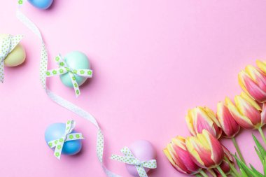 Paskalya mesajı. Şerit kurdeleli renkli yumurta, bahar laleleri, Mutlu Paskalya dekorasyonunda pastel pembe arka planda tüyler. Folyo minimalist yumurta tasarımı, modern üst görünüm şablonu