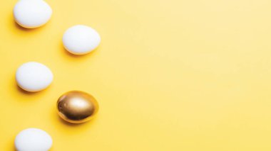 Paskalya sınırı. Mutlu Paskalya dekorasyonunda pastel sarısı arka planda altın, beyaz renkli yumurta. Düz yatış, üst görünüm