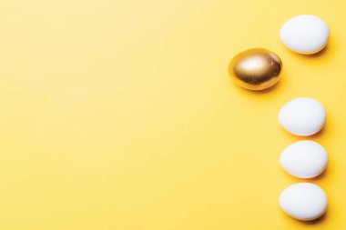 Paskalya sınırı. Mutlu Paskalya dekorasyonunda pastel sarısı arka planda altın, beyaz renkli yumurta. Düz yatış, üst görünüm