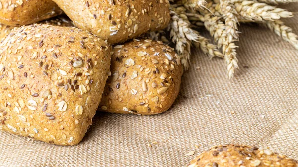 Whole wheat bread. Fresh loaf of rustic traditional bread with wheat grain ear or spike plant on linen texture background. Rye bakery with crusty loaves and crumbs. Homemade baking