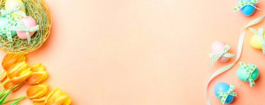 Paskalya tavşanı. Bant kurdeleli renkli yumurta, bahar laleleri, Mutlu Paskalya dekorasyonunda pastel pembe arka planda tüyler. Üst görünümde geleneksel pankart