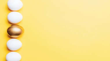 Paskalya sınırı. Mutlu Paskalya dekorasyonunda pastel sarısı arka planda altın, beyaz renkli yumurta. Düz yatış, üst görünüm