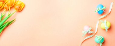 Paskalya tavşanı. Bant kurdeleli renkli yumurta, bahar laleleri, Mutlu Paskalya dekorasyonunda pastel pembe arka planda tüyler. Üst görünümde geleneksel pankart