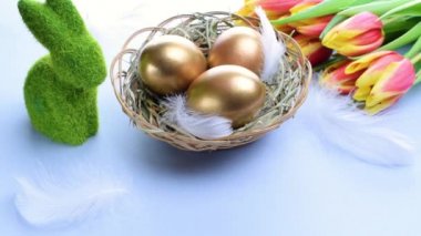 Yumurta rengi. Mutlu Paskalya süslemeleri: sepetteki altın renkli yumurtalar bahar laleleri, pastel mavi arka planda beyaz tüyler. Folyo minimalist yumurta tasarımı, modern şablon