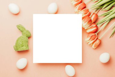 Bahar laleli Paskalya yumurtası sepette, pastel pembe arka planda beyaz tüyler Mutlu Paskalya süslemesinde. Düzlükte şenlikli dekorasyon