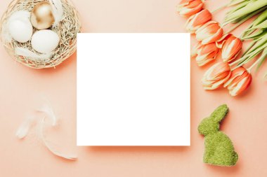 Paskalya sepeti. Bahar laleleriyle sepetin içinde altın, beyaz yumurta, Mutlu Paskalya dekorasyonunda pastel pembe arka planda tüyler. Kopyalama alanı olan folyo minimalist yumurta tasarımı