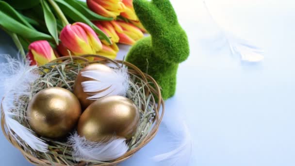 复活节彩蛋复活节快乐装饰 金蛋在篮子里 有春天的郁金香 白色羽毛在淡蓝色的背景上 阳光下的传统装饰 — 图库视频影像