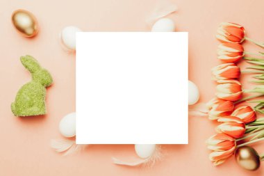 Paskalya bayrağı. Bahar laleleriyle sepetin içinde altın, beyaz yumurta, Mutlu Paskalya dekorasyonunda pastel pembe arka planda tüyler. Folyo minimalist yumurta tasarımı, modern üst görünüm şablonu