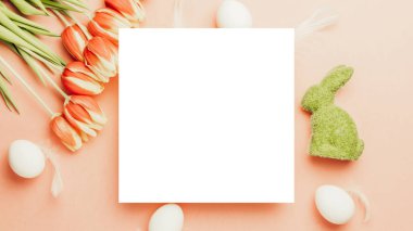 Paskalya kartı. Bahar laleleriyle sepetin içinde altın, beyaz yumurta, Mutlu Paskalya dekorasyonunda pastel pembe arka planda tüyler. Düz konum, kopyalama alanı olan üst görünüm