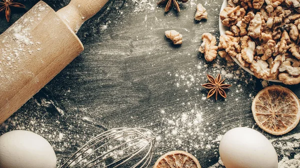 Bakery background frame. Fresh food ingredients: flour, eggs, nut and star anise, orange on black chalkboard background for bread. Still life captured from above, top view, flat lay