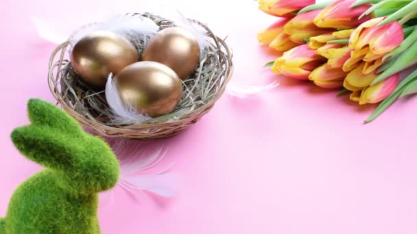 复活节彩蛋黄金金黄色的蛋 篮子里有春天的郁金香 白色的羽毛 粉红的背景 装饰着复活节快乐 恭喜你的复活节设计 — 图库视频影像
