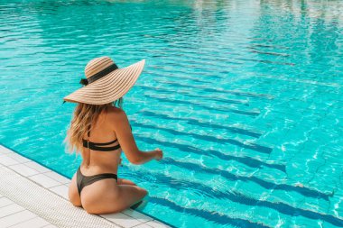 Yaz eğlencesi plajı. Hasır şapkalı, bikinili, mavi havuzda yüzen güneş gözlüklü seksi bir kadın. Kaplıca ve güneşlenme açık havada