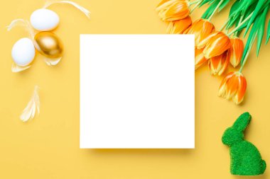 Paskalya laleleri. Bahar laleleriyle sepetin içinde altın, beyaz yumurta, Mutlu Paskalya dekorasyonunda pastel sarısı arka planda tüyler. Üst görünümde geleneksel tasarım