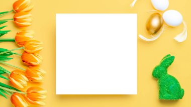 Paskalya çiçeği. Bahar laleleriyle sepetin içinde altın, beyaz yumurta, Mutlu Paskalya dekorasyonunda pastel sarısı arka planda tüyler. Kopyalama alanı olan şenlikli tasarım
