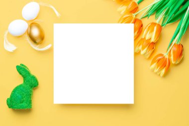 Paskalya sarısı. Bahar laleleriyle sepetin içinde altın, beyaz yumurta, Mutlu Paskalya dekorasyonunda pastel sarısı arka planda tüyler. Düz yatış, üst görünüm