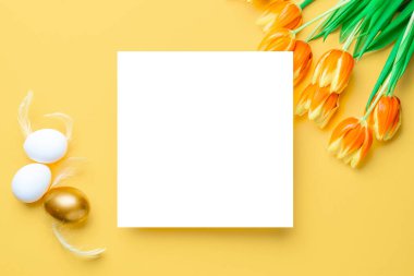 Yumurta rengi. Mutlu Paskalya süslemeleri: sepetteki altın renkli yumurtalar bahar laleleri, pastel sarısı arka planda beyaz tüyler. Folyo minimalist yumurta tasarımı, modern üst görünüm şablonu