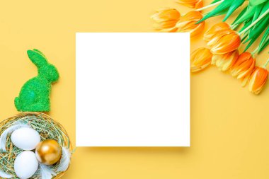 Paskalya lüksü. Bahar laleleriyle sepetin içinde altın, beyaz yumurta, Mutlu Paskalya dekorasyonunda pastel sarısı arka planda tüyler. Düz yatış, üst görünüm