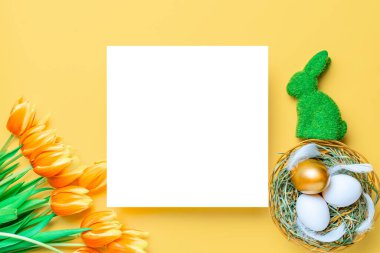 Sepet paskalya süslemesi: İlkbahar laleli altın yumurta, pastel sarısı arka planda beyaz tüyler. Kutlama paskalya tasarımı. Üst görünüm