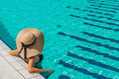 Yüzme havuzu tatili. Bikini mayo, güneş gözlüğü ve mavi sudaki hasır şapkalı mutlu genç seksi kız. Yaz tatilinde spa tatil beldesinde