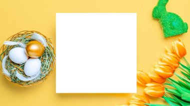 Paskalya yumurtası. Mutlu Paskalya süslemeleri: sepetteki altın yumurtalar bahar laleleri, pastel sarısı arka planda beyaz tüyler. Geleneksel güneş ışığı dekorasyonu. Üst görünüm