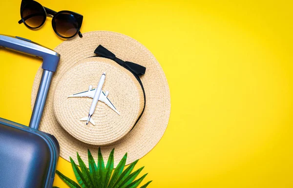 Summer time. Travel accessories with suitcase, white plane, palm leaves in minimal trip vacation concept on yellow background. Exotic tropical beach with copy space