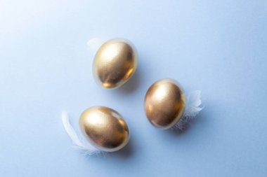 Mutlu Paskalya süslemelerinde pastel mavi arka planda beyaz tüylü altın Paskalya yumurtası sepeti. Bahar tatili üst görünüm kavramı