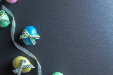 Paskalya arka planı mavi. Mutlu Paskalya dekorasyonunda koyu kaba taştan arka planda bant şeritli renkli yumurta. Düz yatış, üst görünüm